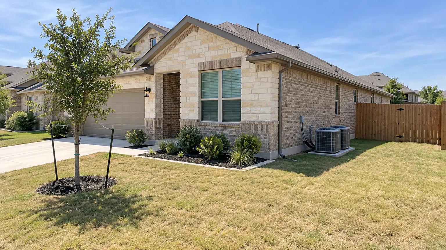 Two outdoor AC condenser units beside a newer limestone and brick house in Central Texas sun.